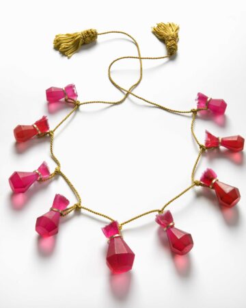 Rubyfruits,  necklace with cast faceted rubies in dyed resin with eyelets in 18 carat gold, gathered in a gold-coloured silk thread with passementerie. 
Ruby likes to travel was the title for my solo exhibition in Gallery Mette Saabye, Copenhagen. It was an exhibition of ruby jewellery - not real rubies but rubies cast in resin. When visiting the exhibition the visitor could borrow any piece of the jewellery for a day. Each piece has a small suitcase and a logbook to go with it and the only requirement for borrowing the piece was to document the day in the logbook with a few photos and a text.
Photo Dorte Krogh